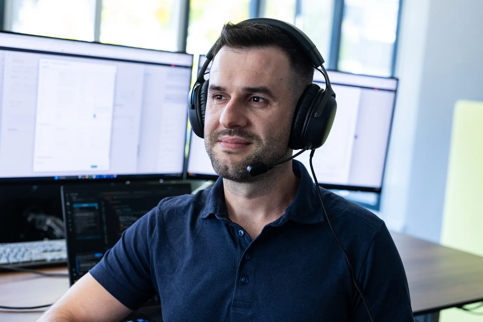 Mitarbeiter mit Headset an einem Arbeitsplatz mit mehreren Bildschirmen