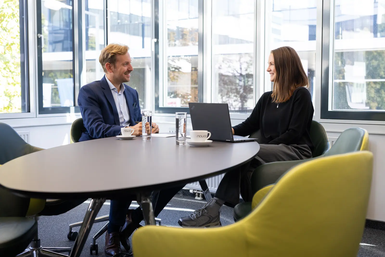 Zwei Personen im Gespräch an einem runden Besprechungstisch mit Laptop
