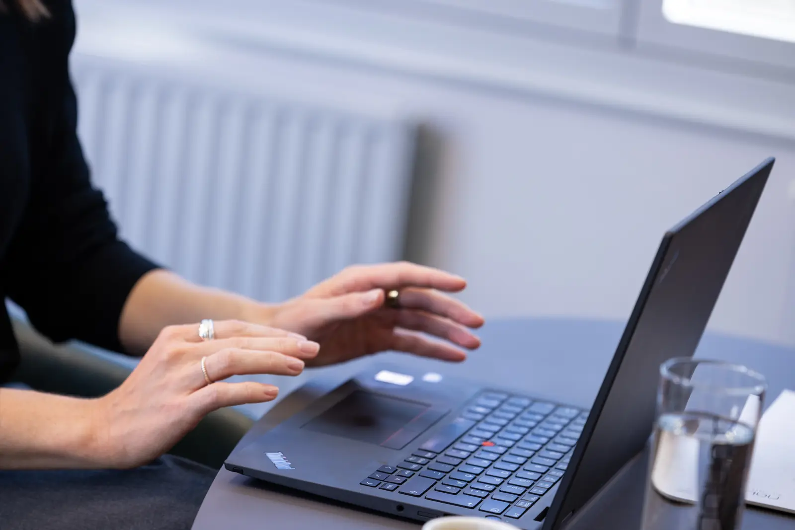 Hands on a laptop keyboard, a glass of water next to it