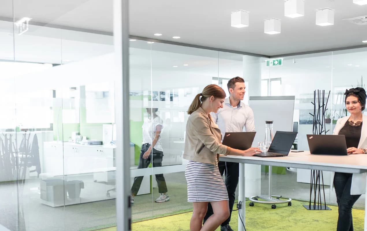 Projektteam an einem Stehtisch mit Laptops in einem hellen Besprechungsraum