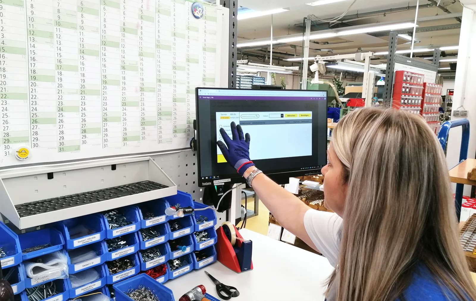 An employee taps a screen showing the production app at her workstation