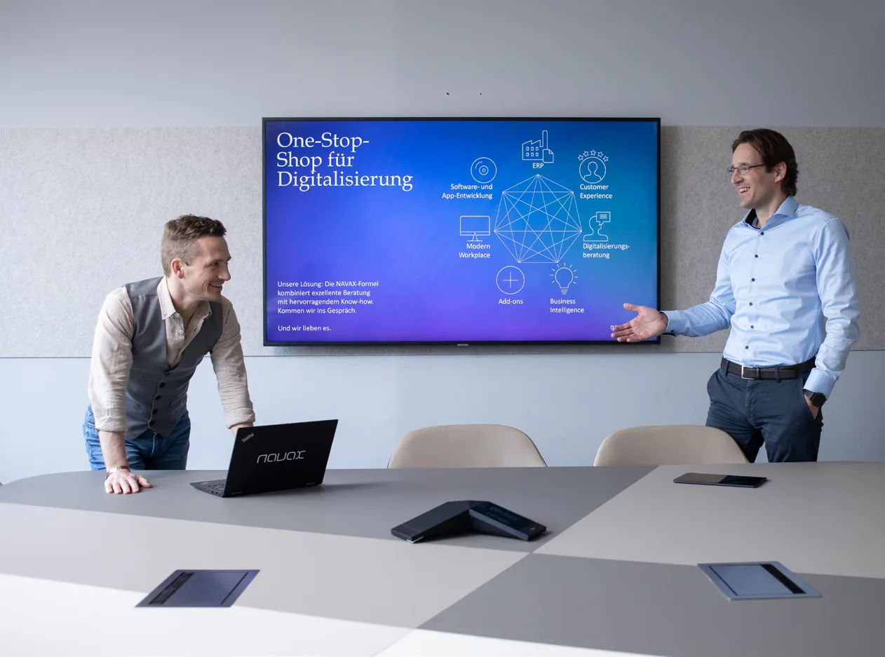 Zwei Personen in einem Besprechungsraum vor einem Bildschirm mit der Folie „One-Stop-Shop für Digitalisierung“