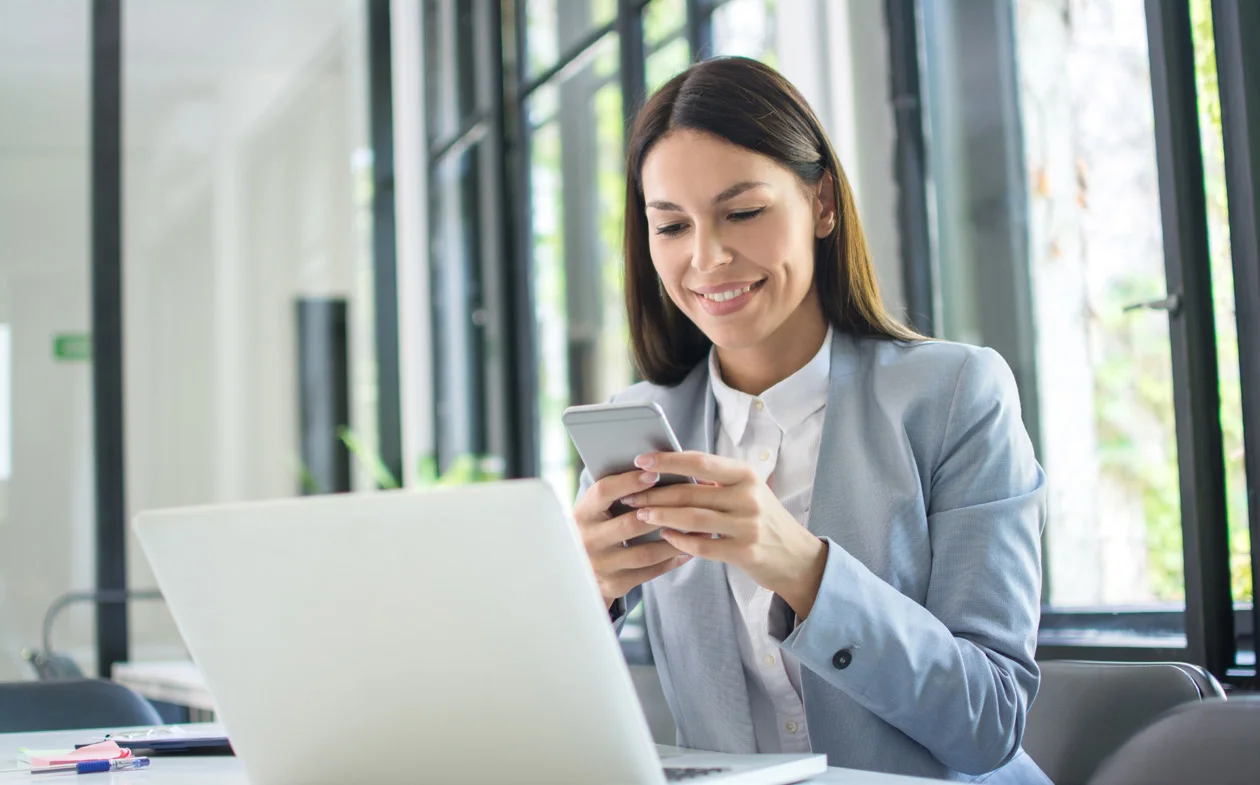 Eine Frau arbeitet mit Smartphone und Laptop in einem hellen Büro