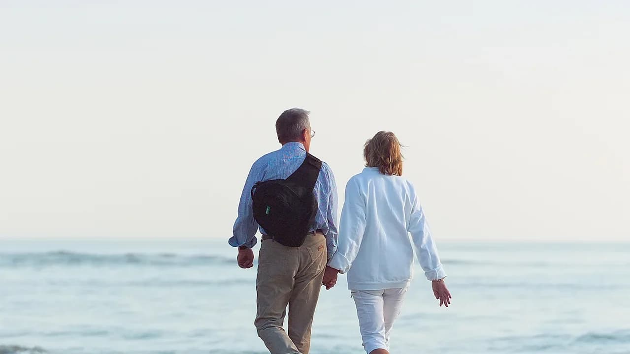 Ein älteres Paar spaziert Hand in Hand am Meer