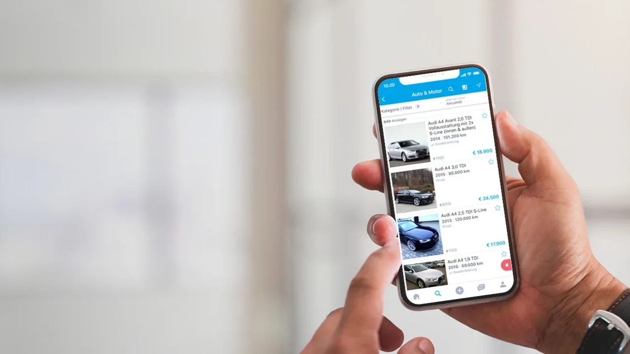 Hand holding a smartphone showing listings in the Auto & Motor category of the willhaben app