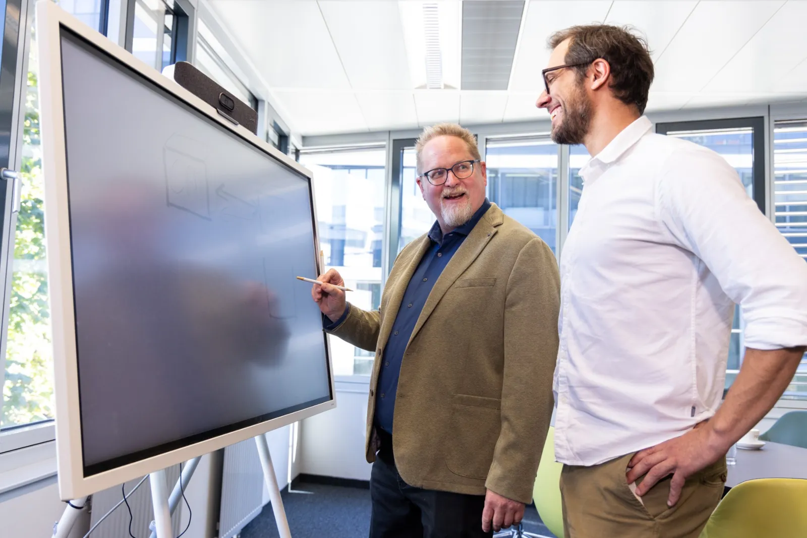 A consultant sketching on a digital whiteboard, a colleague watching and laughing