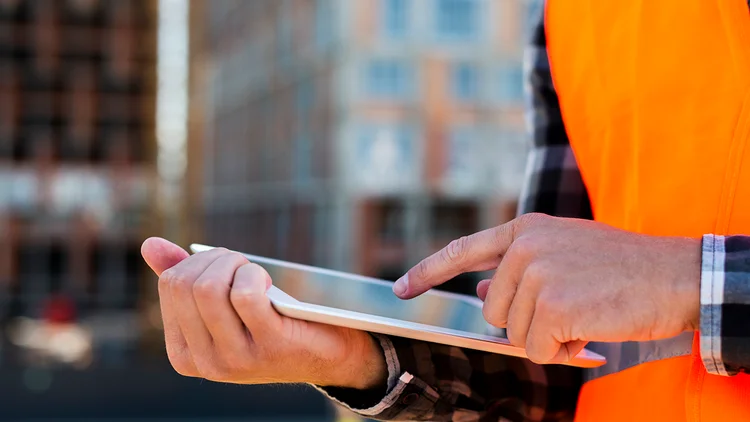 Mann auf Baustelle hÀlt Laptop in der Hand und analysiert die LiquiditÀt