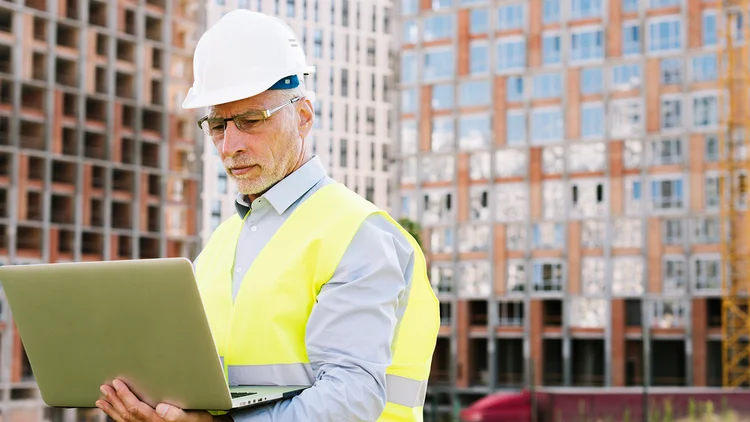 Mann hÀlt Laptop in der Hand und arbeitet auf Baustelle