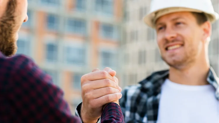 Zwei junge MÀnner lÀcheln sich an und klatschen auf Baustelle ein