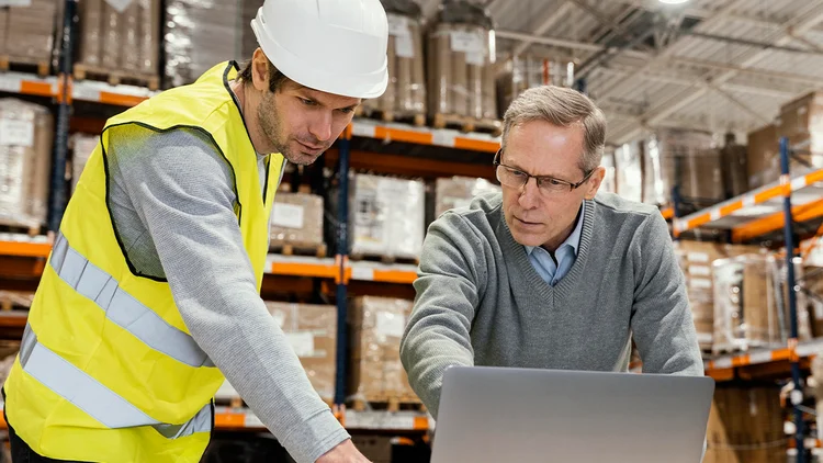 Zwei Männer arbeiten im Lager und analysieren etwas auf einem Laptop
